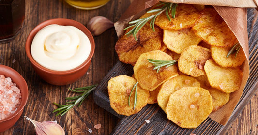 Crisp potato chips wrapped in paper and displayed on a wooden charcuterie board. There are bowls of salt and dip beside it.
